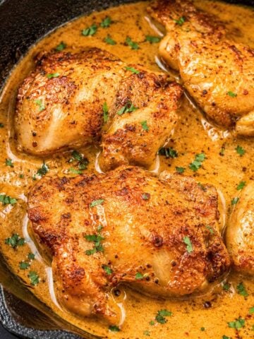 Boneless skinless chicken thighs seared until golden in a cast-iron skillet, simmering in a creamy pan sauce and topped with chopped parsley.