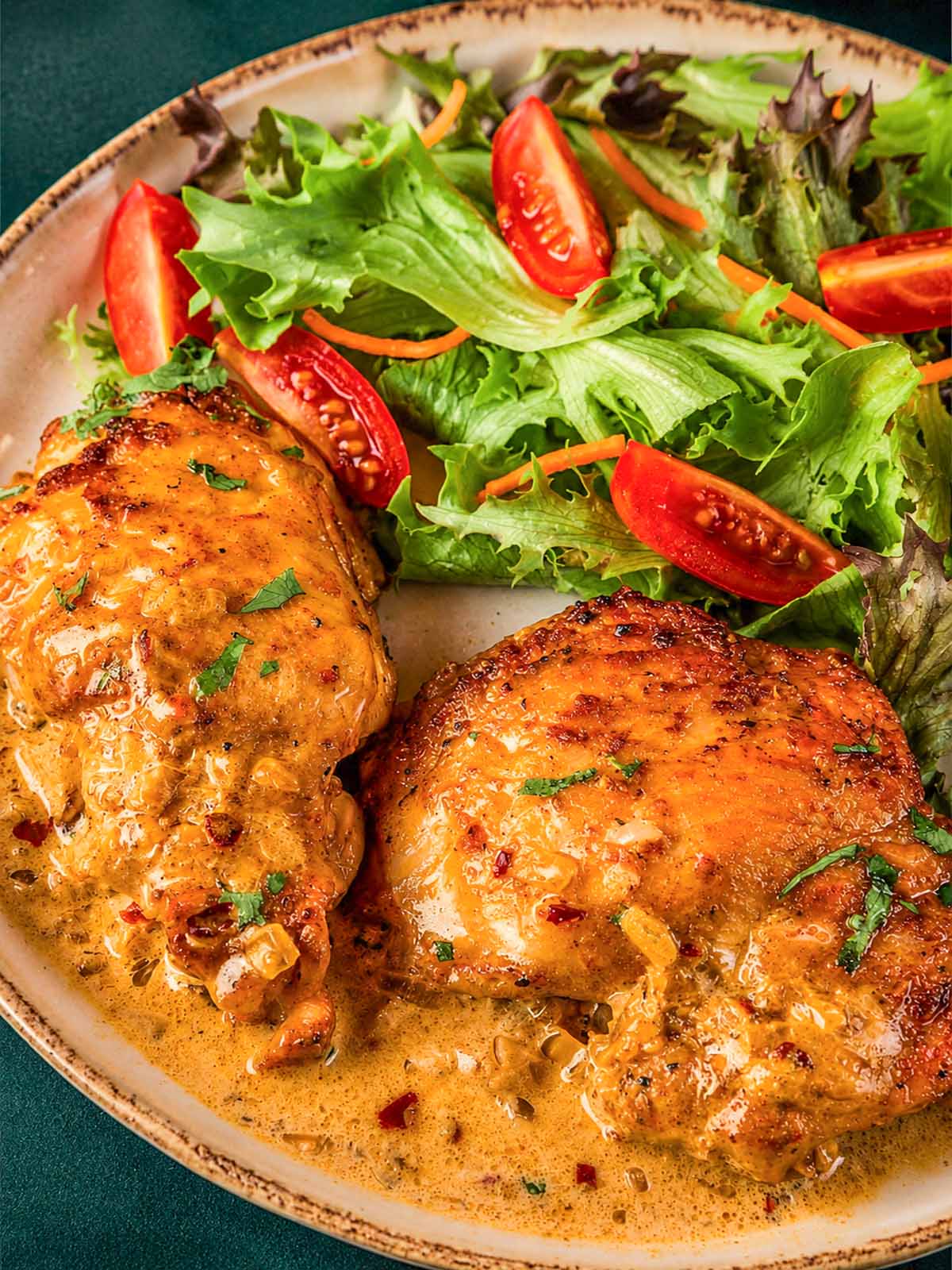 Boneless skinless chicken thighs in a creamy sauce, served on a plate with a fresh green salad and sliced cherry tomatoes.