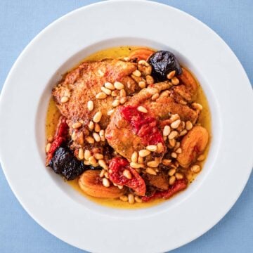 Braised Chicken Thighs with Prunes and Apricots served in a white bowl, topped with toasted pine nuts and simmered in a rich sauce with tender dried fruit.