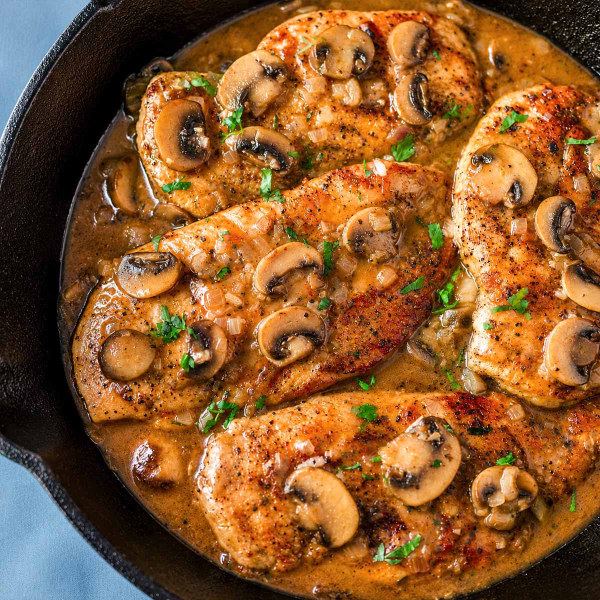 Chicken Marsala without cream in a skillet with sautéed mushrooms, onions, and a glossy Marsala wine sauce, finished with parsley.