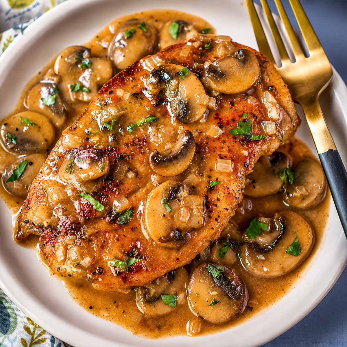 Chicken Marsala without cream served on a plate with sliced mushrooms, diced onions, and a glossy Marsala wine sauce, finished with parsley.