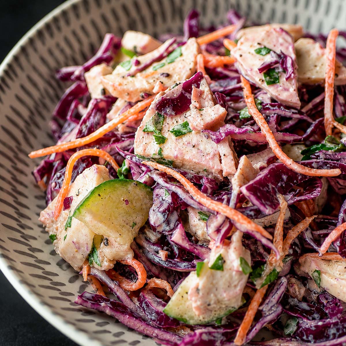 Close up Creamy chicken cabbage salad with red cabbage, cucumber, carrot, and tender chicken pieces in a light dressing