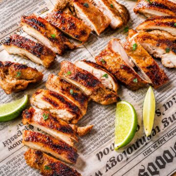 Sliced chipotle chicken thighs with charred edges and lime wedges on a parchment-lined tray.