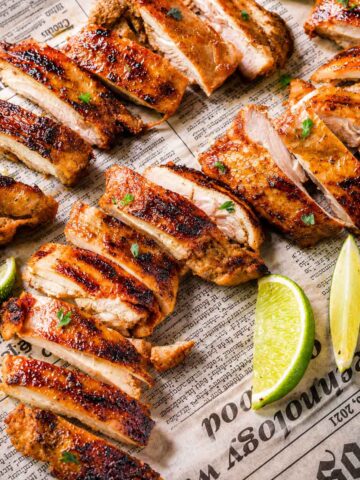 Sliced chipotle chicken thighs with charred edges and lime wedges on a parchment-lined tray.
