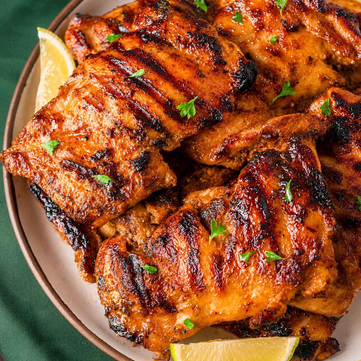 Chipotle chicken thighs with a smoky charred crust, fresh parsley, and lime wedges on a plate.