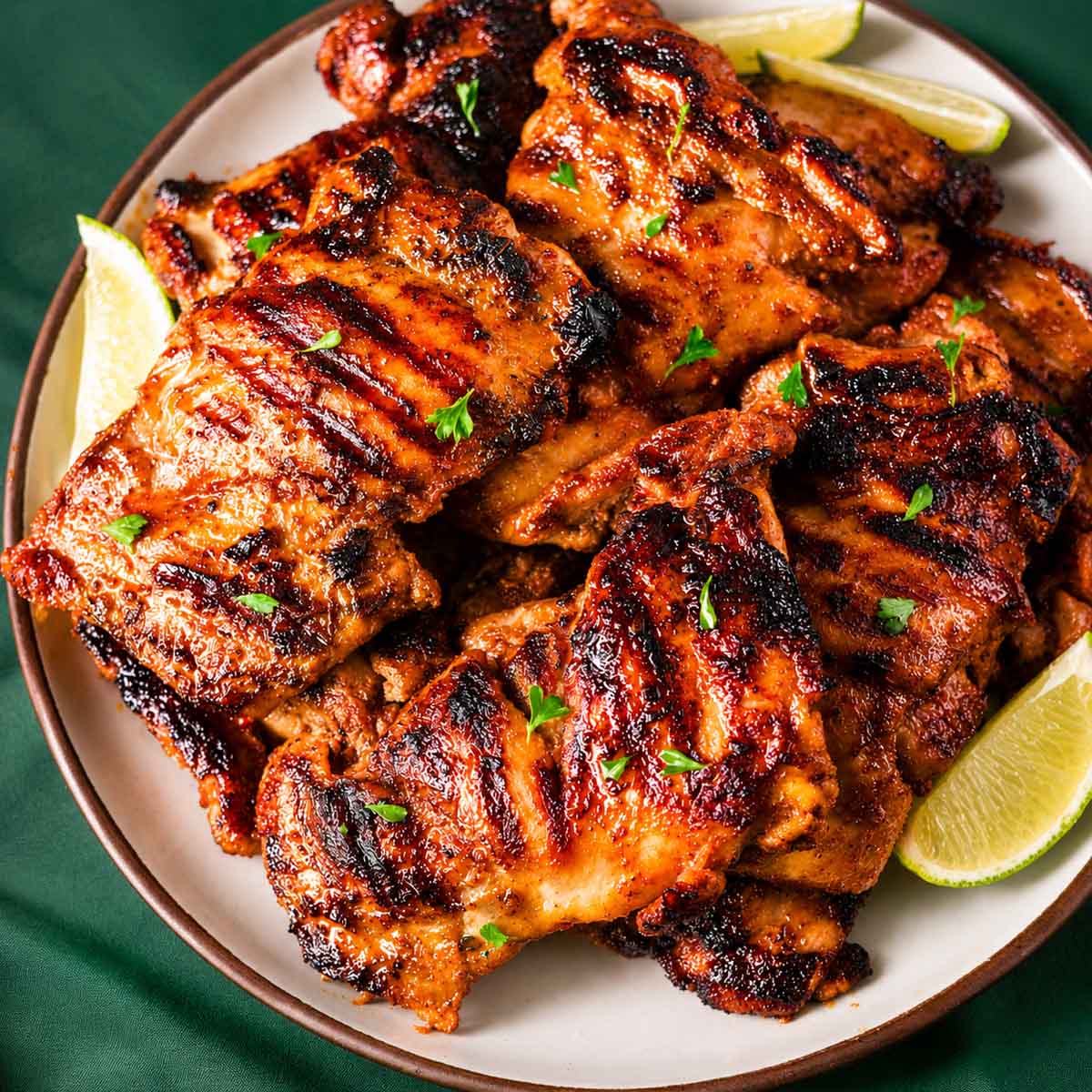 Grilled chipotle chicken thighs with caramelized char marks, parsley, and lime wedges.