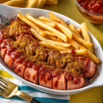Currywurst with crispy fries topped with rich curry ketchup sauce and curry powder