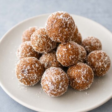 Close up Date and Walnut Energy Balls (Easy No-Bake Snack) dusted with coconut on a white plate.