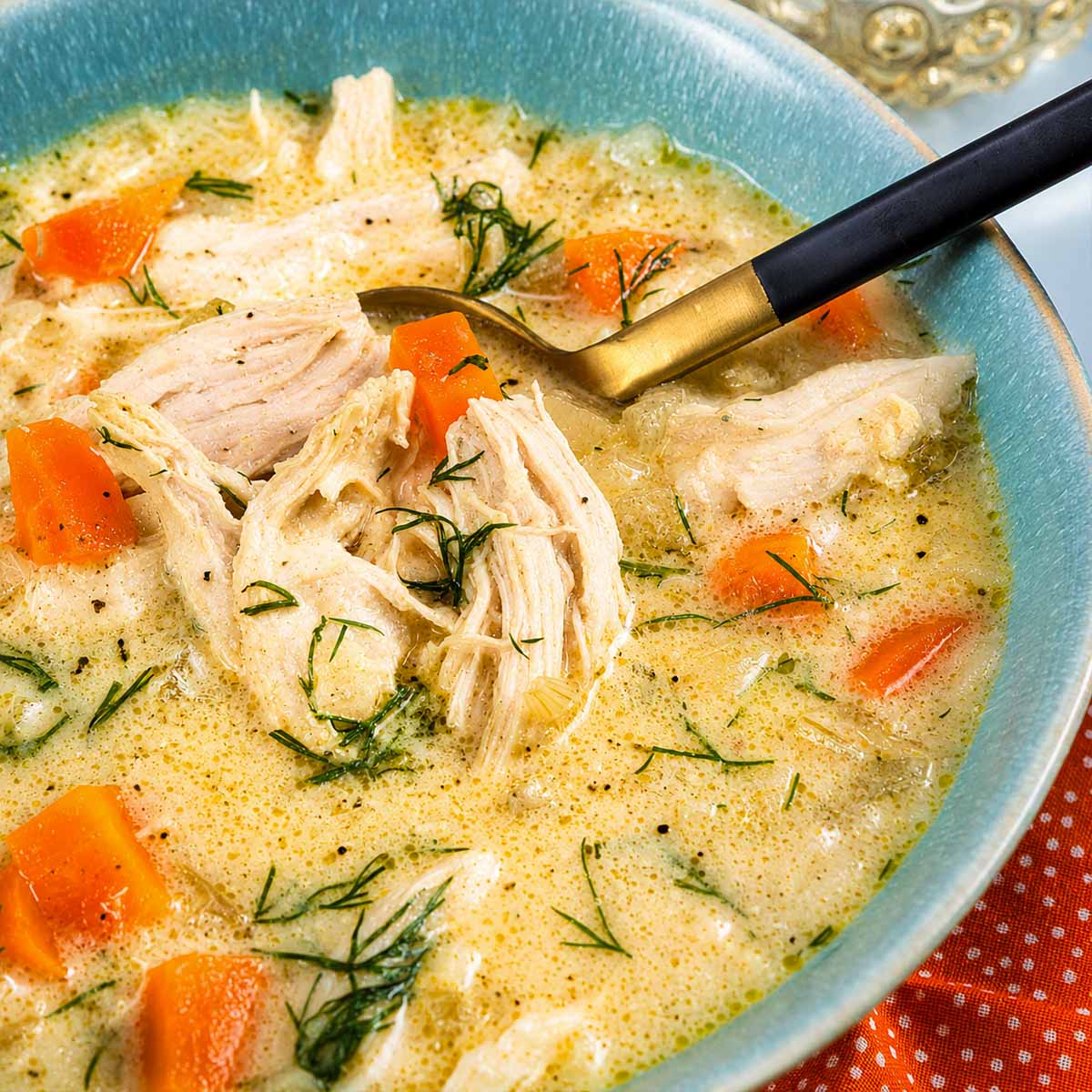 Close-up of Greek lemon chicken soup with orzo (avgolemono) with shredded chicken, carrots, celery, and dill in a creamy lemon broth.