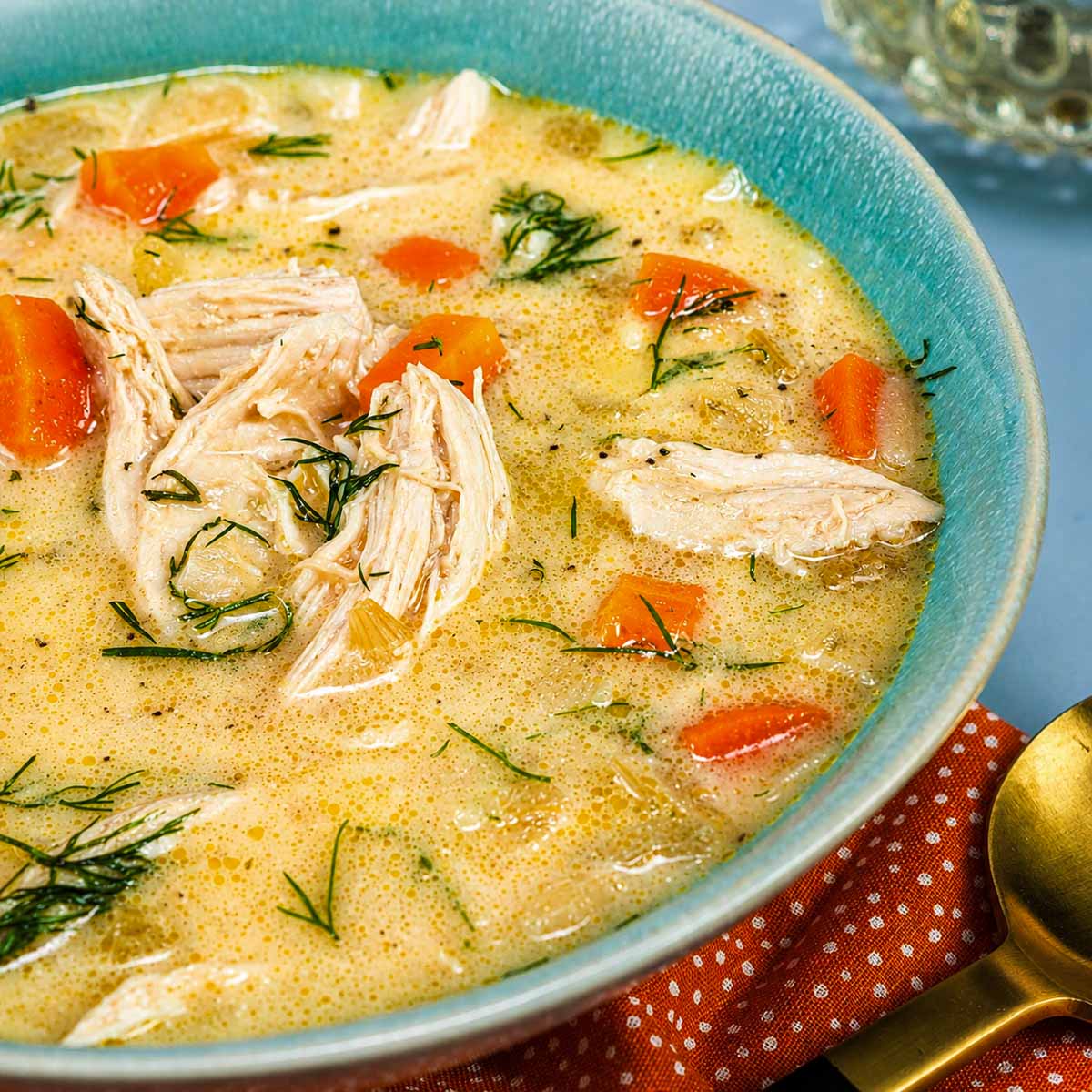 Bowl of Greek lemon chicken soup with orzo (avgolemono) topped with shredded chicken, carrots, celery, and fresh dill.