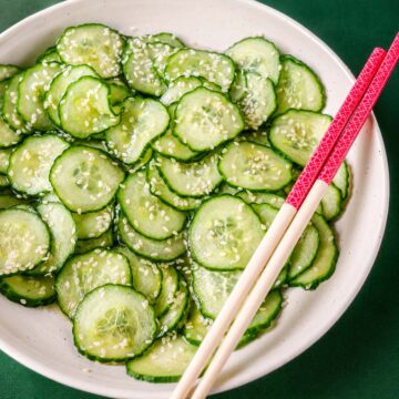Close-up of Japanese cucumber salad (sunomono) with thin cucumber slices in a light vinegar dressing, sprinkled with sesame seeds, with chopsticks resting on the bowl.
