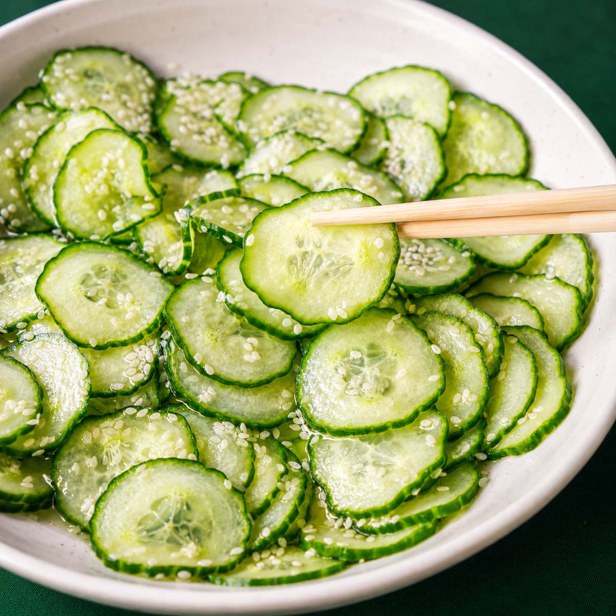 Chopsticks lifting a thin cucumber slice from Japanese cucumber salad (sunomono) with sesame seeds in a light vinegar dressing.
