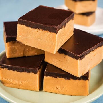 Peanut butter bars with a smooth dark chocolate topping stacked on a plate