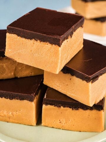 Peanut butter bars with a smooth dark chocolate topping stacked on a plate