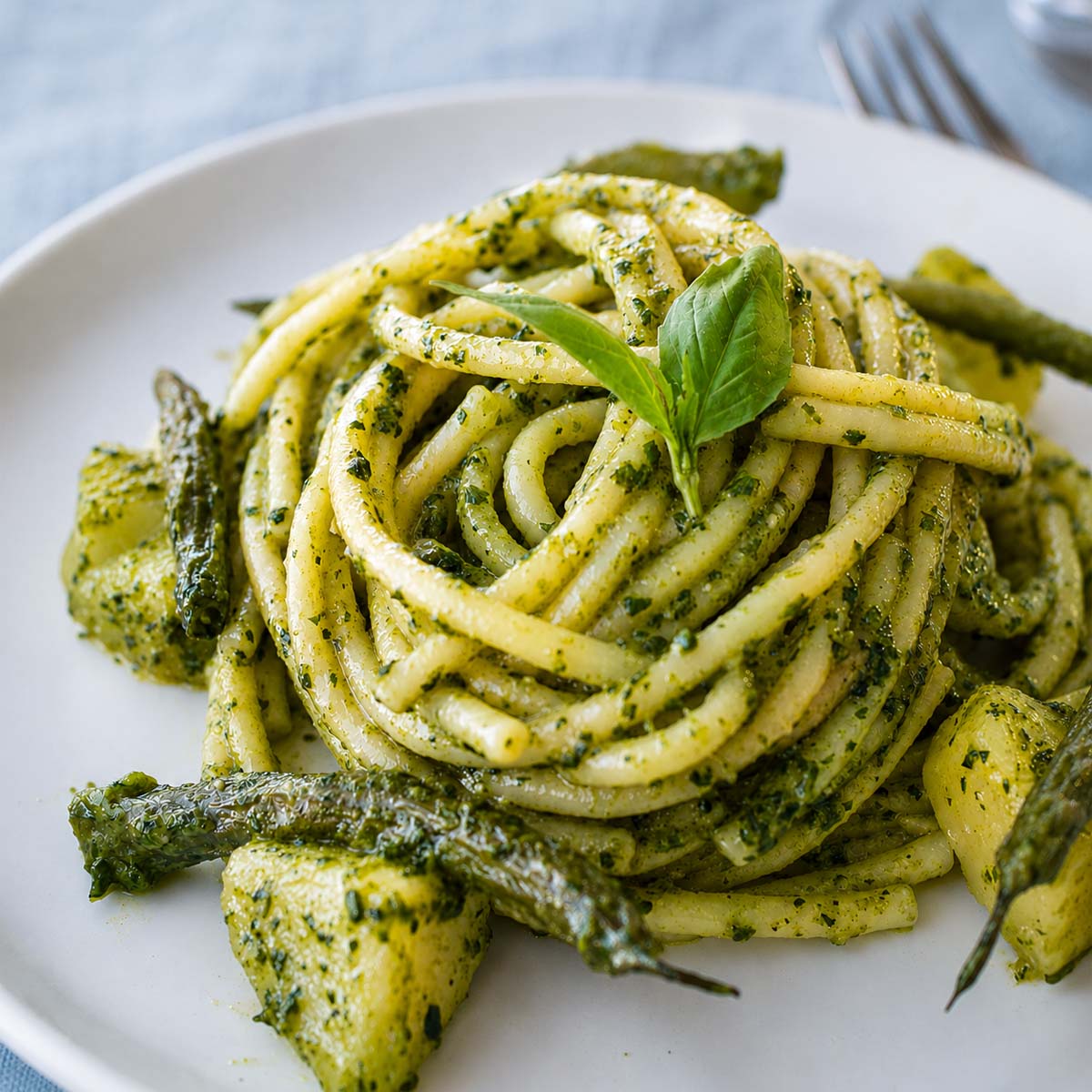 Pesto pasta with potatoes and green beans topped with fresh basil on a white plate
