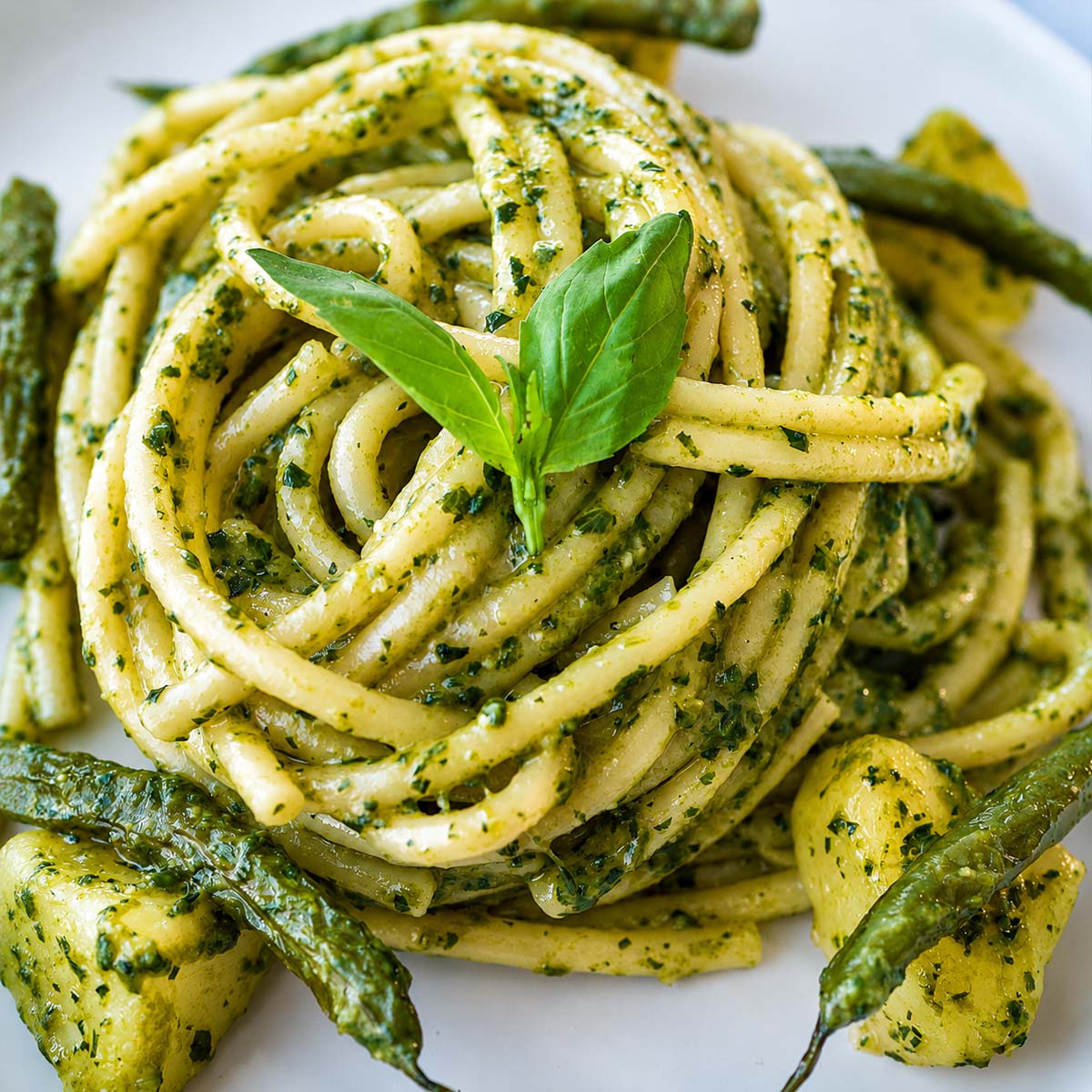 Italian pesto pasta with tender potatoes, green beans, and fresh basil pesto on a white plate.