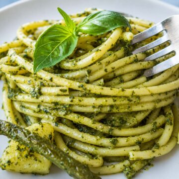 close up Pesto pasta with potatoes and green beans topped with fresh basil on a white plate