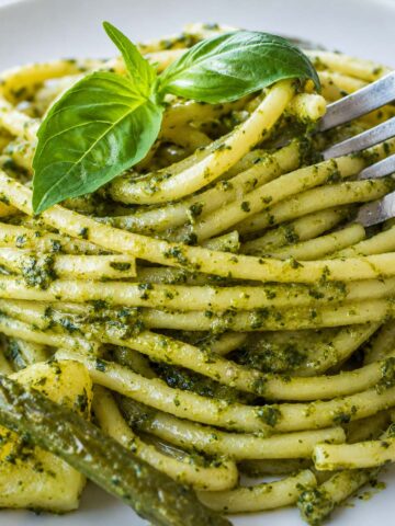 close up Pesto pasta with potatoes and green beans topped with fresh basil on a white plate