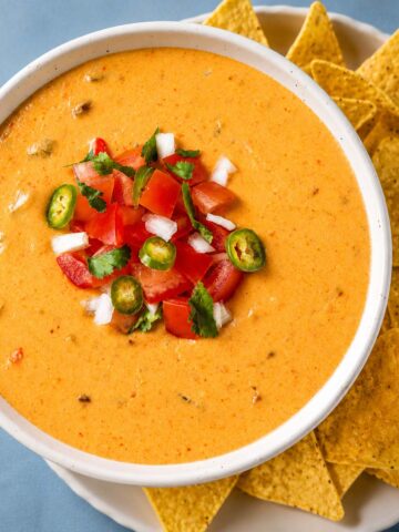 Creamy queso dip topped with diced tomatoes, jalapeño slices, onion, and cilantro, served with tortilla chips.