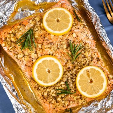 Baked salmon in foil topped with lemon slices, fresh rosemary, and garlic butter, ready to bake for a moist, flaky oven salmon dinner.