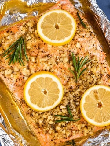 Baked salmon in foil topped with lemon slices, fresh rosemary, and garlic butter, ready to bake for a moist, flaky oven salmon dinner.