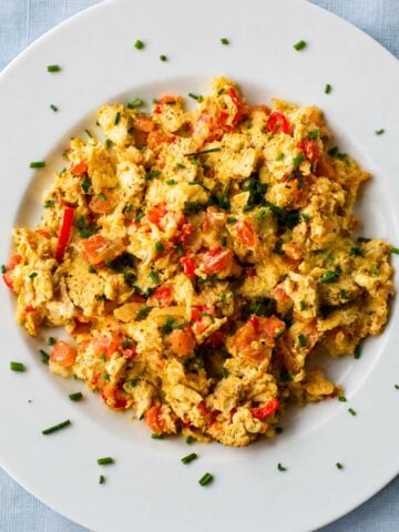 Scrambled eggs with tomatoes, onions, and fresh chives on a white plate