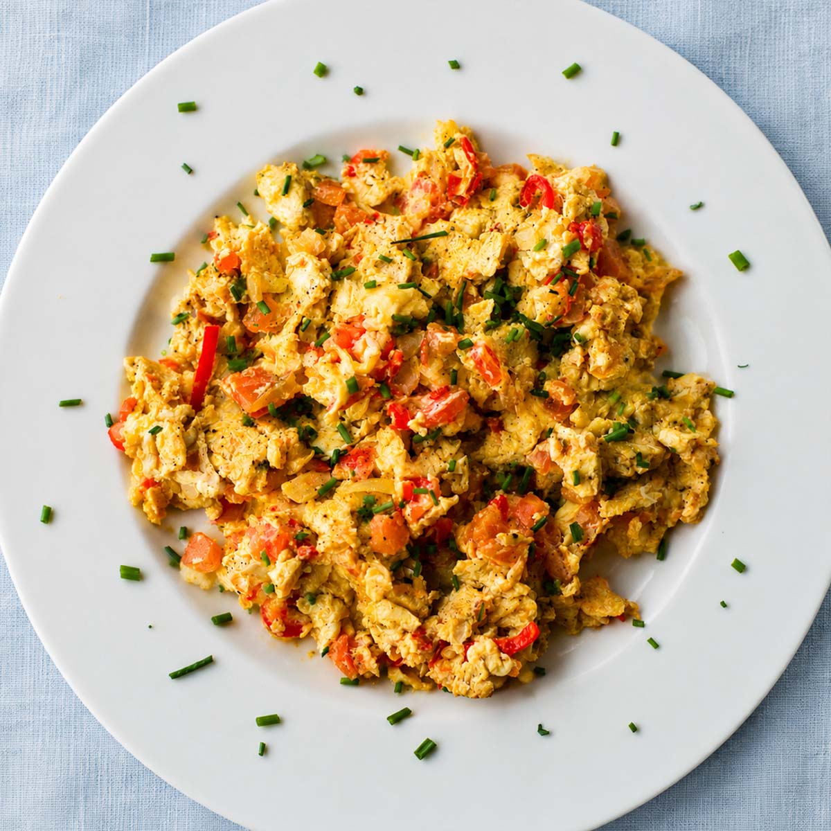 Scrambled eggs with tomatoes, onions, and fresh chives on a white plate