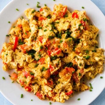 close up Scrambled eggs with tomatoes, onions, and fresh chives on a white plate
