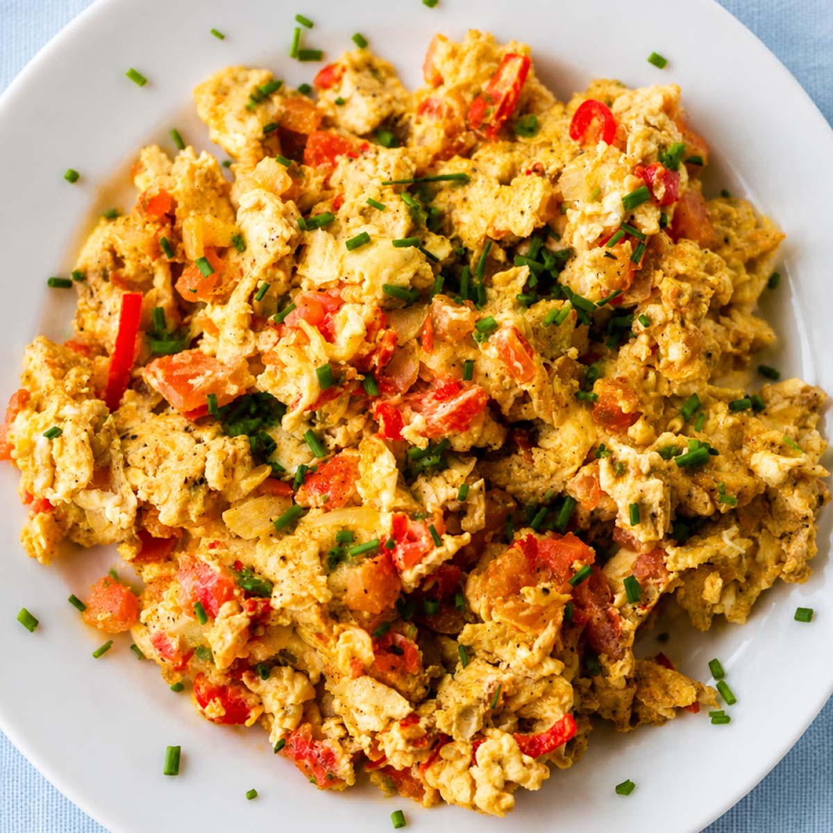 Close up scrambled eggs with tomatoes, onions, and fresh chives on a white plate