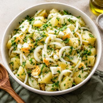 Spanish potato salad made with tender potatoes, sliced onions, hard-boiled eggs, fresh parsley, olive oil, and vinegar dressing