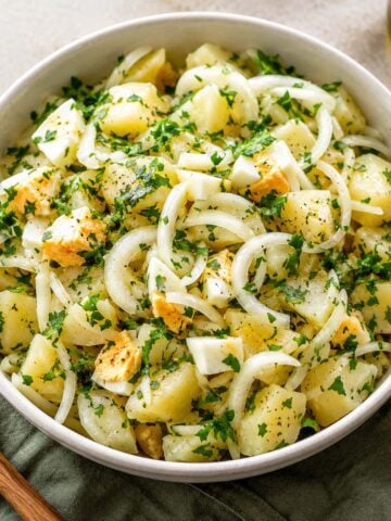 Spanish potato salad made with tender potatoes, sliced onions, hard-boiled eggs, fresh parsley, olive oil, and vinegar dressing