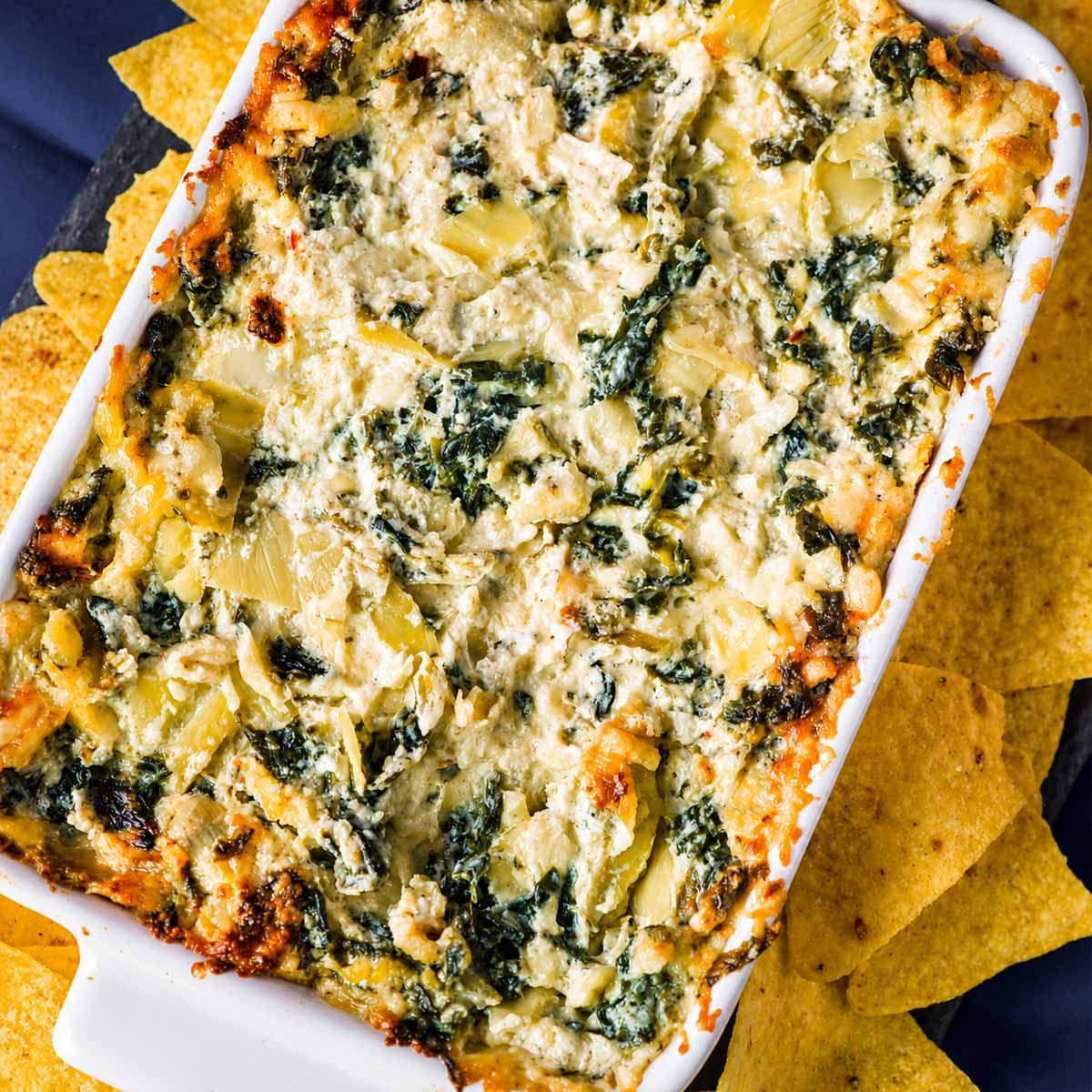 Spinach artichoke dip in a white baking dish with tortilla chips, showing the layers of spinach and creamy dip