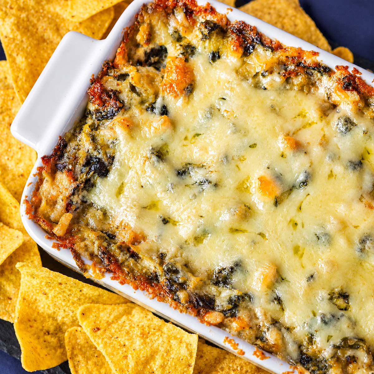 Spinach artichoke dip in a white baking dish with tortilla chips.