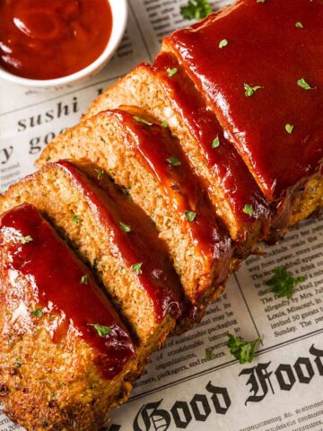Sliced turkey meatloaf with brown sugar ketchup glaze, served on a cutting board with parsley and a small bowl of brown sugar ketchup glaze.