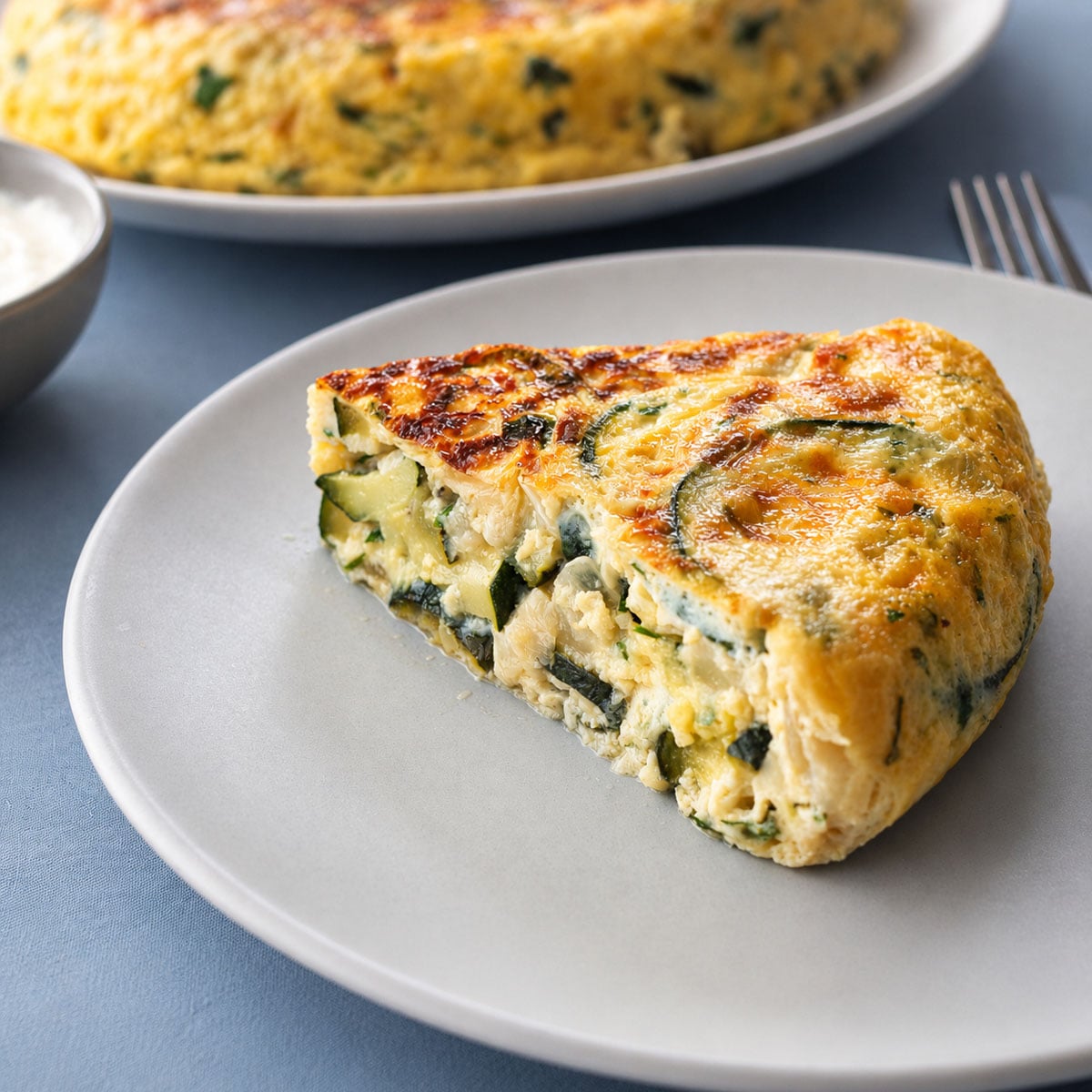 Slice of Zucchini Frittata with Cheese on a White Plate, Showing a Creamy Egg and Zucchini Filling