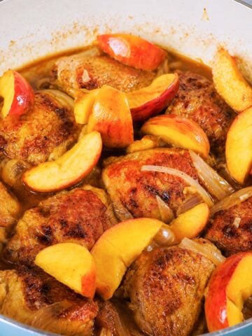 Apple cider chicken thighs with apples and onions simmering in a glossy skillet sauce