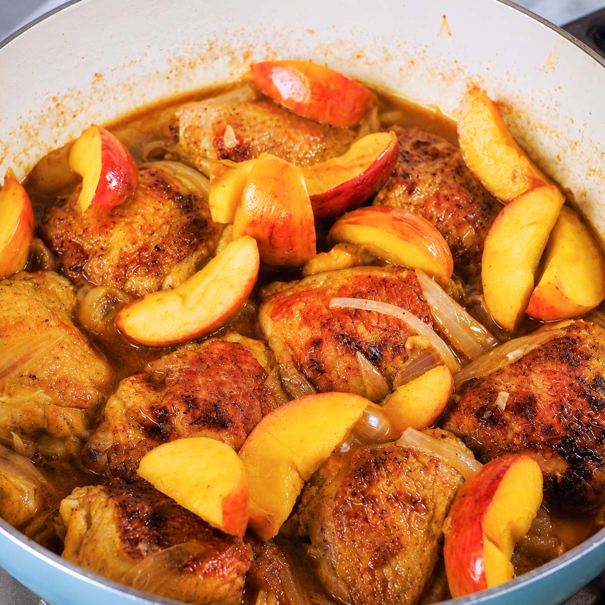 Apple cider chicken thighs with apples and onions simmering in a glossy skillet sauce