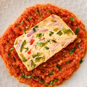 Overhead view of baked frittata with ham, zucchini and bell peppers served over red pepper sauce