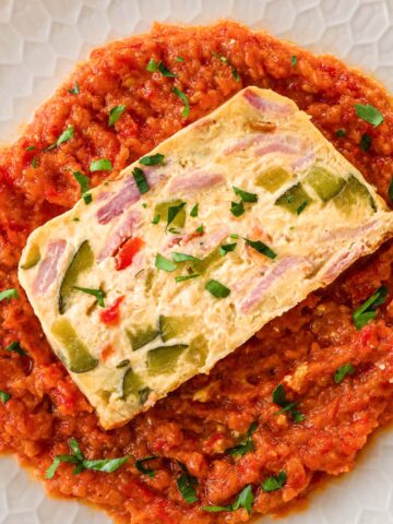 Overhead view of baked frittata with ham, zucchini and bell peppers served over red pepper sauce