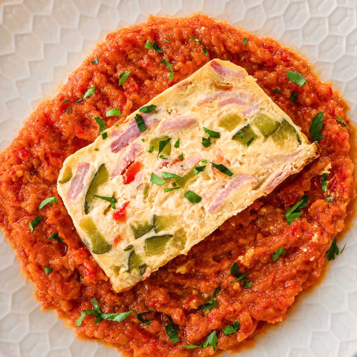 Overhead view of baked frittata with bacon and vegetables served over red pepper sauce