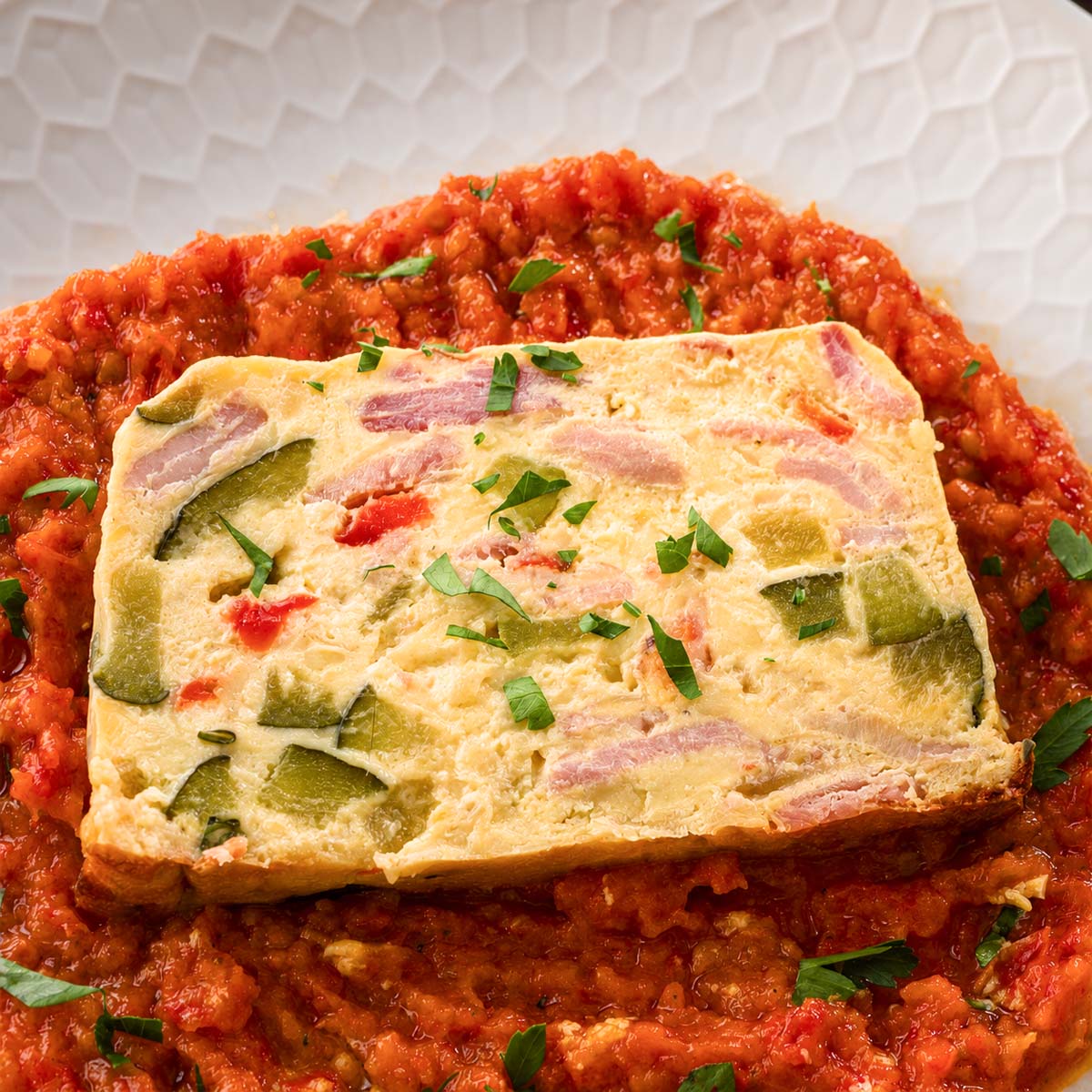 Close-up of a baked frittata slice with bacon and vegetables served with red pepper sauce