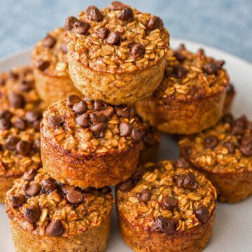 Banana oatmeal chocolate chip muffins stacked on a plate with a soft blue-gray background