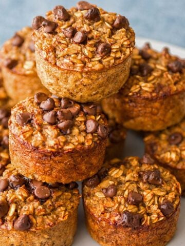 Banana oatmeal chocolate chip muffins stacked on a plate with a soft blue-gray background