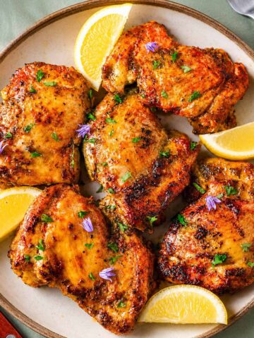 Boneless skinless chicken thigh marinade with grilled chicken thighs, fresh lemon wedges, and parsley on a ceramic plate