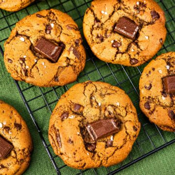 Brown butter chocolate chip cookies with melted chocolate chunks and flaky sea salt on a cooling rack.