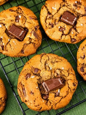 Brown butter chocolate chip cookies with melted chocolate chunks and flaky sea salt on a cooling rack.