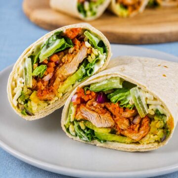 Buffalo chicken wraps cut in half with lettuce, avocado, carrots, shredded cheese, and creamy ranch dressing