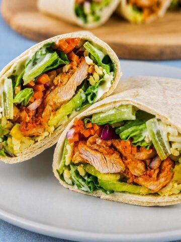 Buffalo chicken wraps cut in half with lettuce, avocado, carrots, shredded cheese, and creamy ranch dressing