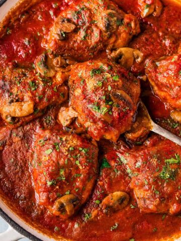 Chicken Marengo simmering in a skillet with mushrooms in a rich tomato and white wine sauce
