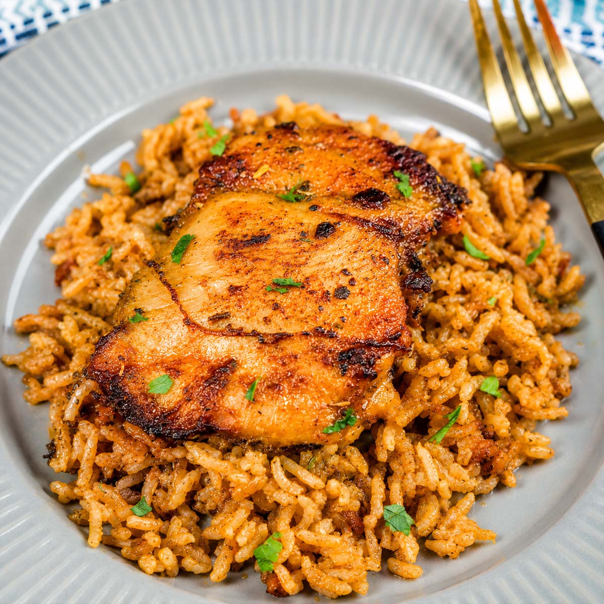 Plate of baked chicken thighs served over seasoned rice, garnished with parsley, with a fork on the side.
